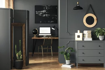 Fotobehang Per kamer Wooden cupboard with fresh plant and books standing in the real photo of open space living room interior with wainscoting on wall and desk with computer and black globe  © Photographee.eu