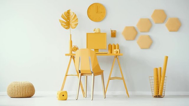 Bright yellow home office interior with desk, computer, chair, pouf and clock on white wall. Cinemagraph video of plush dice.