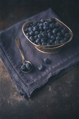 Fototapeta na wymiar Freshly Picked Blueberries in Silver Basket; Some Blueberries in Silver Spoon; Deep Blue Napkin on Black Background