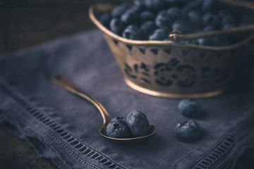Freshly Picked Blueberries in Silver Basket; Some Blueberries in Silver Spoon; Deep Blue Napkin on Black Background