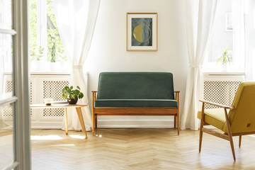 Green sofa with dark, wooden frame and a comfy yellow armchair in a white retro living room...