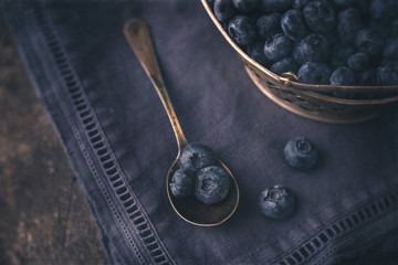 Freshly Picked Blueberries in Silver Basket; Some Blueberries in Silver Spoon; Deep Blue Napkin on Black Background