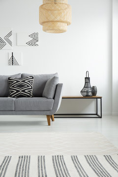 Real photo of a simple living room interior with gray couch, monochromatic paintings, rattan lamp and wooden table