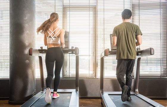 Full Length Rear View Of Young Man And Woman Running On Treadmills During Workout Session At The Gym