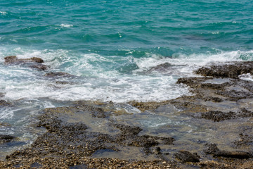 sea foam of the surf on the pebble beach shore. clear water in the stone gaps