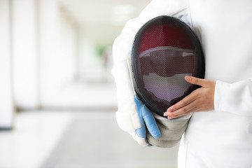 Close-up of a fencer in white fencing suit and hand holding her mask.