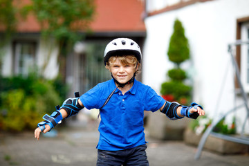 Portrait of little school kid boy in safety protection clothes scating with rollers. Active sporty...