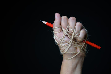 Hand with red pencil tied with rope, depicting the idea of freedom of the press or freedom of...