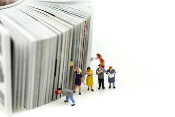 Miniature people: Businessman reading newspaper and sitting on book using as background education or business concept.