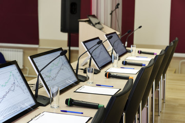 Conference room table for business meeting with microphones, monitors, pens, papers, glasses for water and chairs in row, selective focus 