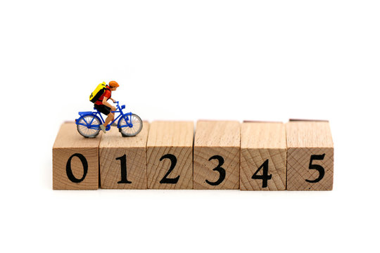 Miniature people : Travelers riding bicycle on wooden block number using as background traveling concepts.