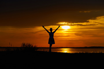 Happy woman hands up against the sunset.