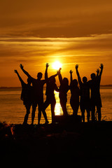 Group of happy friends hands up against the sunset.
