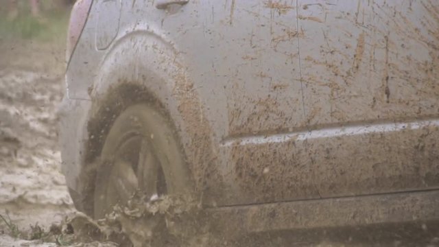 Powerful white SUV leaves a dirty puddle. Beautiful view of the car outside the city. Extreme driving and rest conditions in bad weather. From under the wheels on the grass flying waves of dirt and