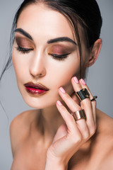 portrait of beautiful girl with closed eyes posing with golden rings on hand, isolated on grey