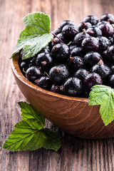 Big wooden bowl with fresh black currant and original leaves on wooden background close-up