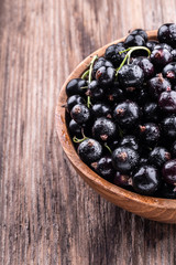 Half of big wooden bowl with fresh black currant on wooden background close-up.