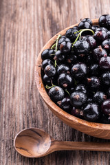 Half of big wooden bowl with fresh black currant and spoon on wooden background close-up.