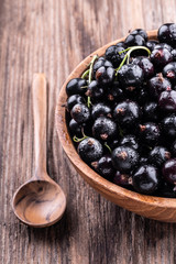 Half of big wooden bowl with fresh black currant and spoon on wooden background close-up.