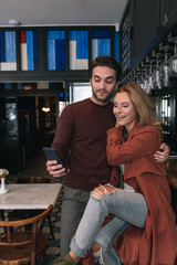 Valuable memory. Cheerful glad couple using phone and hugging