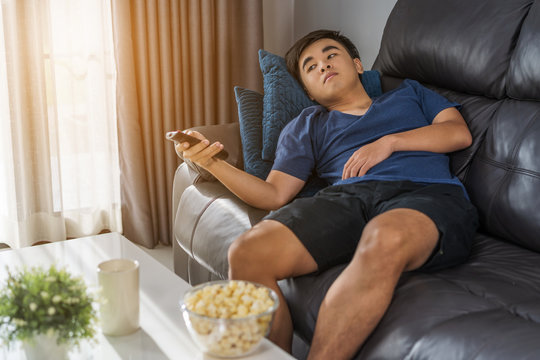 man holding remote control and watching TV while sitting on sofa in the living room