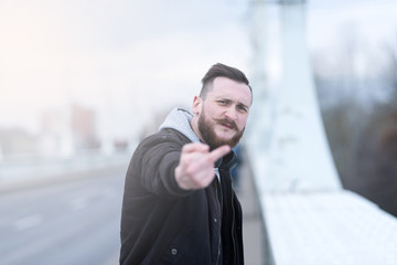A handsome young hipster man showing his middle finger to the camera in an urban environment.