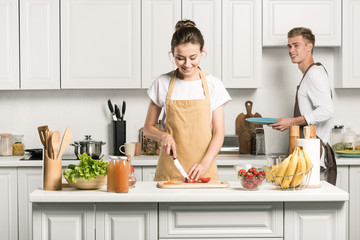 girlfriend cooking salad and cutting tomatoes in kitchen