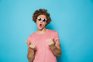 Portrait of stylish handsome man 20s with brown curly hair wearing modern glasses pointing fingers...