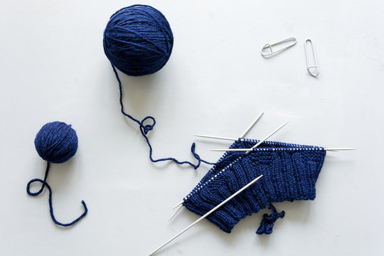 Girl knits blue hat knitting needles on gray wooden background. Process of knitting. Top view. Flat lay