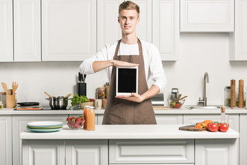 handsome young man holding tablet with blank screen in kitchen
