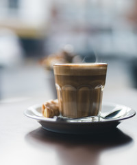 coffee in a glass cup with a small cannoli with blurry background 