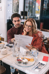 Tasty dishes. Satisfied focused couple choosing meal and sitting at table