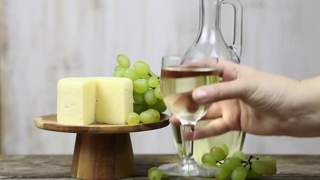 Woman's hand with a glass of wine on a background of grapes and cheese. Woman nils and drinks wine.