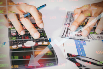 Business man or accountant in gray shirt holding pen working on accounts and using calculator and writing on desk, With sunset light.
