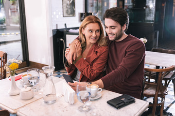 On date. Energetic jovial couple sitting at restaurant and using phone