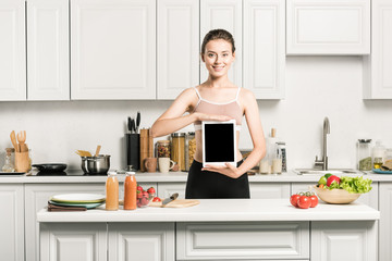 Obraz na płótnie Canvas attractive girl in sport bra holding tablet with blank screen in kitchen