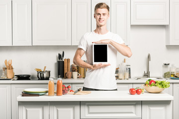 handsome young man holding tablet with blank screen in kitchen