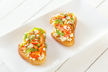 Two Bruschettes with red sweet pepper and goat cheese in a plate on white boards
