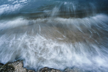Lubricated small waves with foam during the beginning of the storm in the evening on the shore of the dark sea at the beach of a sea resort photographed for long exposure