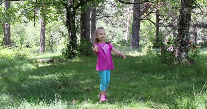 Four years old blonde girl standing on the grass playing with frisbee, in a forest of the countryside. 4k video.
