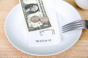 Plate with fork upside down indicating finished with meal, mug beside, bill receipt on plate. For...