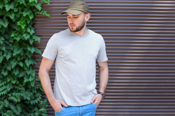 Young man wearing gray t-shirt near wall on street. Urban style