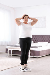 Overweight woman in sportswear using scales in bedroom