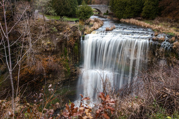 Waterfall in Autumn. A Stone Bridge across the River is Visible in Background.