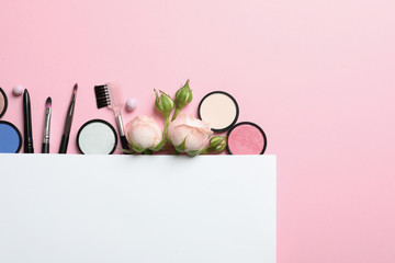 Flat lay composition with card and products for decorative makeup on pastel pink background