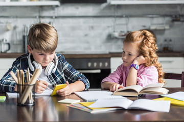 Fototapeta premium concentrated little kids doing homework together at kitchen