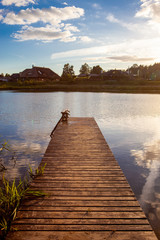 Obraz premium Piękne drewniane molo z chmurami i słońcem odbijające się w spokojnej i błękitnej wodzie