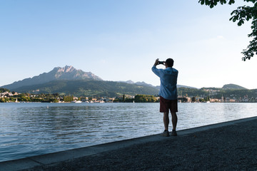 Back side silhoutte view of alone man standing on the embankment, making a photo on the phone Mount luzern, Switzerland
