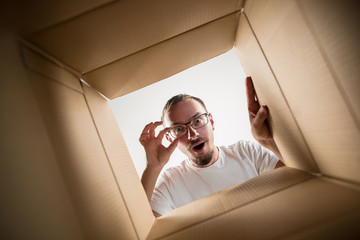 The surprised man unpacking, opening carton box and looking inside. The package, delivery,...