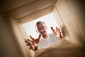 The surprised man unpacking, opening carton box and looking inside. The package, delivery, surprise, gift lifestyle concept. Human emotions and facial expressions concepts - obrazy, fototapety, plakaty